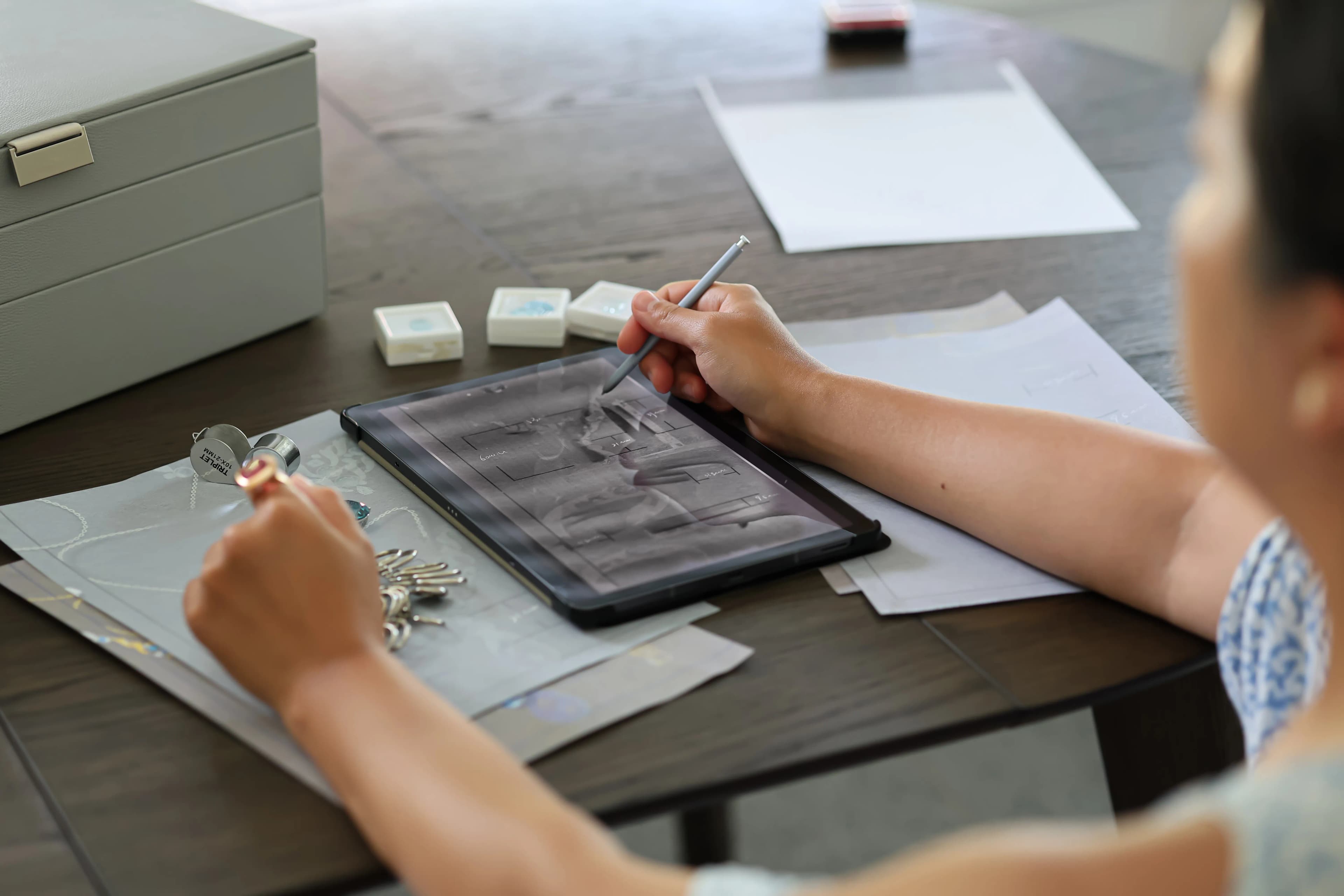 Sereeni designer refining a bespoke jewelry design while examining a gemstone with a loupe